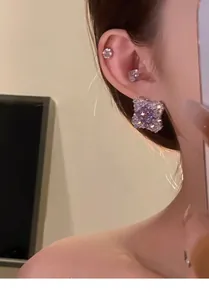 Close-up of sparkling rhomboid zircon stud earrings with silver pins on a female ear