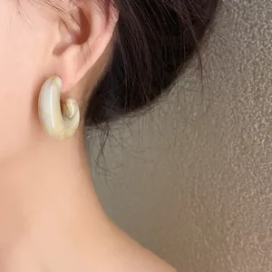 Close-up of a C-shaped acrylic earring with marble pattern on a model's ear