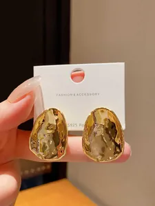 Close-up of golden irregular textured metal stud earrings with S925 silver posts.