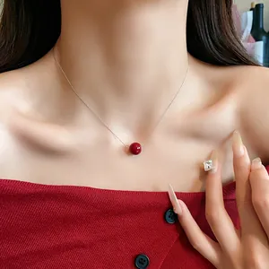 Detail view of a minimalist red pearl pendant necklace on a silver chain worn by a model