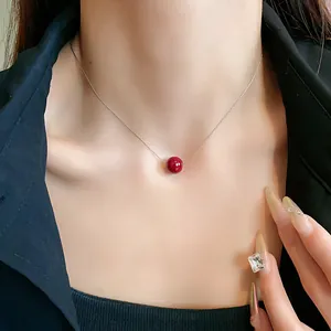 Close-up of a minimalist red pearl pendant on a silver chain worn by a woman.