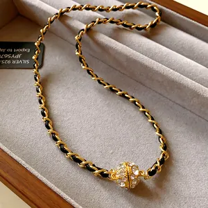 Gros plan sur collier chaîne dorée entrelacée de cuir avec pendentif magnétique en strass