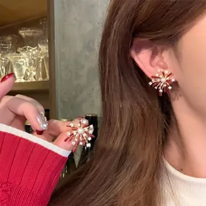 Close-up of fireworks-shaped pearl stud earrings with red accents and zircons on ear.