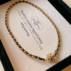 Détail du collier chaîne dorée gainé de cuir avec boule magnétique ornée de strass brillants.