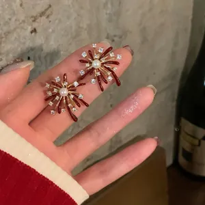 Close-up view of elegant firework-shaped stud earrings with red enamel and central pearls