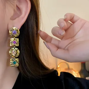 Close-up detail of vintage gold-tone drop earrings with colorful gemstones on a model