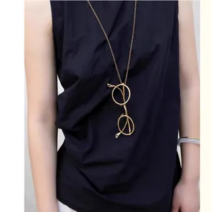 Gold-finish glasses pendant necklace on a model wearing navy blue. Elegant detail.