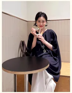 Asian model wearing a stylish metallic glasses pendant necklace in a cozy cafe setting.