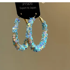 Dettaglio ravvicinato di grandi orecchini a cerchio con paillettes a stella blu chiaro.