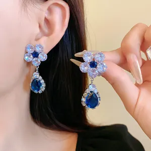 Primo piano di eleganti orecchini in zircone blu con fiori e gocce d'acqua su modella