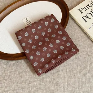 Vintage brown floral print headscarf folded on a wooden tray with a book detail