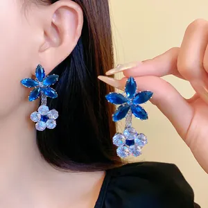 Dettaglio di orecchini a sospensione con fiori in zircone blu e bianco su modella