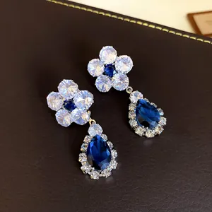 Primo piano di raffinati orecchini a goccia e fiore in zircone blu su pelle scura
