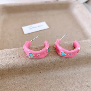 Dettaglio di orecchini a cerchio a C in smalto rosa con pietre blu e strass.