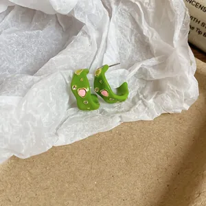 Primo piano di orecchini a cerchio in smalto verde con cuori rosa e strass.