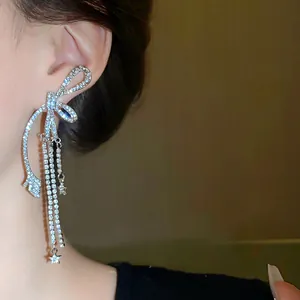 Detailansicht eleganter silberner Schleifen-Quastenohrringe mit funkelnden Strasssteinen.