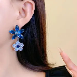 Dettaglio ravvicinato di orecchini pendenti a fiore con cristalli blu e bianchi su una modella