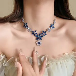 Squisito primo piano di una collana con fiori e foglie in zirconia blu e bianchi su pelle.