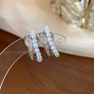 Detailed view of French style pearl and zircon hoop earrings on a transparent display stand