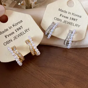 Detail view of 18k gold plated zircon and pearl earrings displayed on cream cards.