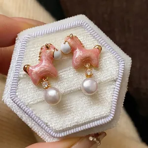 Elegantes pendientes de poni rosa con perlas colgantes y circón, acabado dorado.