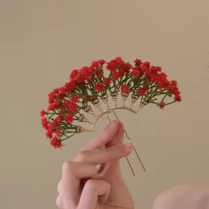 Vue détaillée d'une épingle à cheveux en U tenue à la main avec fleurs rouges artificielles