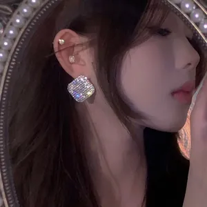 Macro view of elegant square sparkling rhinestone stud earrings worn by a female model