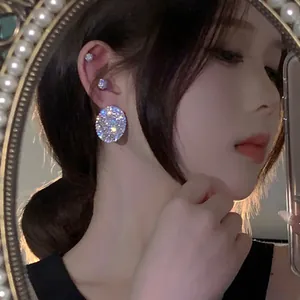 Close-up of a sparkling oval rhinestone earring worn on an ear with a pearl mirror background