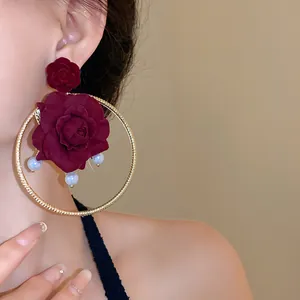 Close-up view of vintage hoop earrings with deep red roses and pearls worn by a model