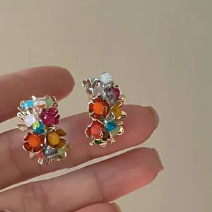 Close-up of colorful floral stud earrings with pearl accents and gold-toned finish