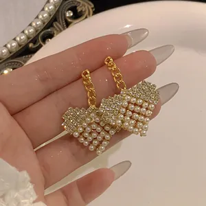 Close-up of heart-shaped earrings with rhinestones and white pearls on a gold chain.