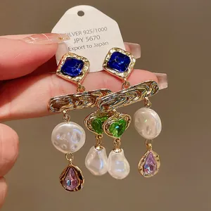 Close-up of vintage earrings with blue and green crystals and baroque pearls.