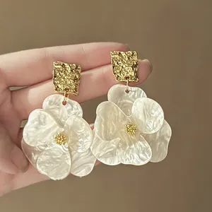Detail of pearl flower earrings with gold textured square studs on beige background