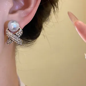 Close-up of a vintage-style earring with a large pearl and rhinestone criss-cross design.