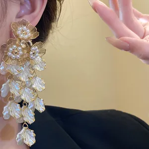 Gros plan de boucles d'oreilles pendantes fleurs dorées avec perles et pétales blancs