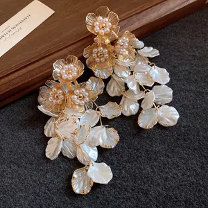 Gros plan d'élégantes boucles d'oreilles fleur dorée avec perles et pétales blancs en cascade