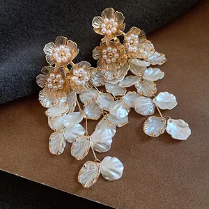 Vue détaillée d'élégantes boucles d'oreilles fleurs dorées avec perles et pétales blancs.