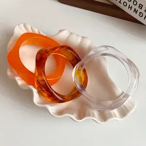 Set of three retro irregular acrylic bangles with marbled and clear finishes in shell tray