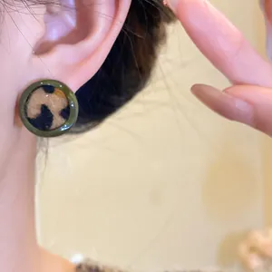 Détail de boucles d'oreilles rondes vintage à motif léopard avec bordure verte sur l'oreille.