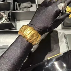 Irregular pleated wide gold cuff bracelet and sphere ring displayed on a black glove