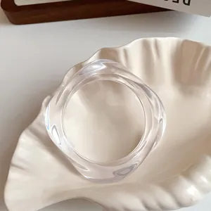 Detailed macro shot of a minimalist clear irregular acrylic wave bangle on a shell dish