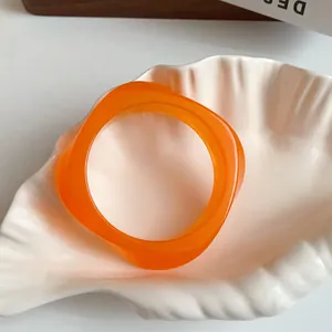 Macro view of a vibrant orange irregular acrylic bangle inside a decorative shell-shaped tray