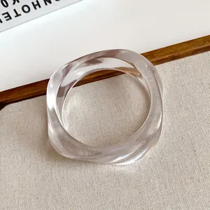 Close-up of a clear acrylic bangle with an irregular wavy design on a textured surface.