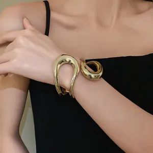 Close-up of chunky gold irregular geometric hollow cross bangle on model's wrist