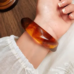 Detailed close-up showing the marbled pattern of the amber acrylic bangle on a wrist