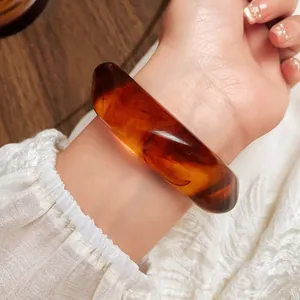 Detailed view of irregular acrylic tortoiseshell marbled bangle on wrist in retro style