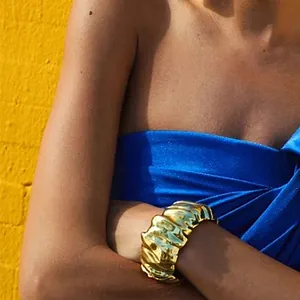 Close-up of wide gold cuff bracelet with irregular crumpled texture on model arm.
