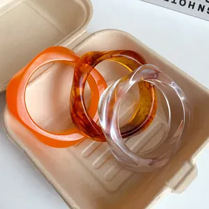 Close-up view of three stylish irregular acrylic bangles in orange, amber, and clear finishes