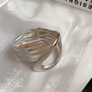 Close-up detail of minimalist silver hollow cross bangle with wavy metallic texture