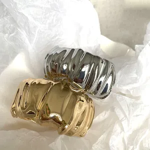 Detailed view of gold and silver irregular pleated wide cuff bracelets on white paper